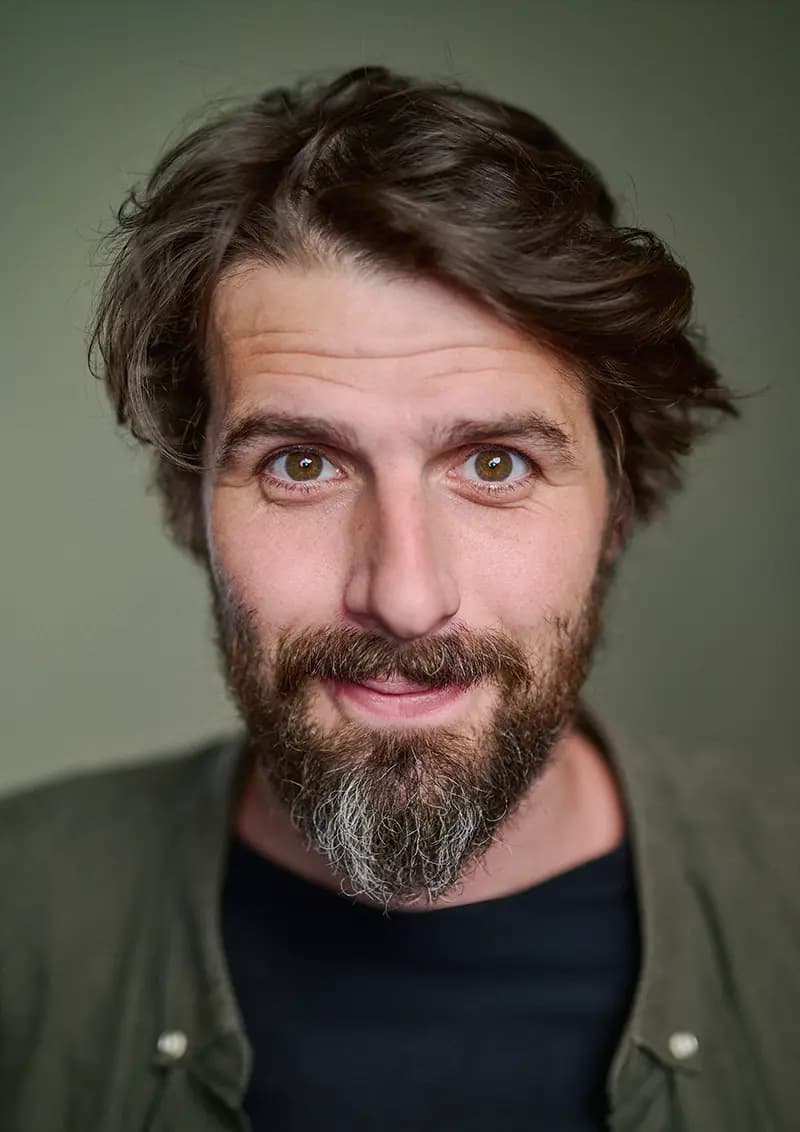 Headshot of actor Henri with a subtle smile, photographed in London studio with soft light and a green canvas backdrop